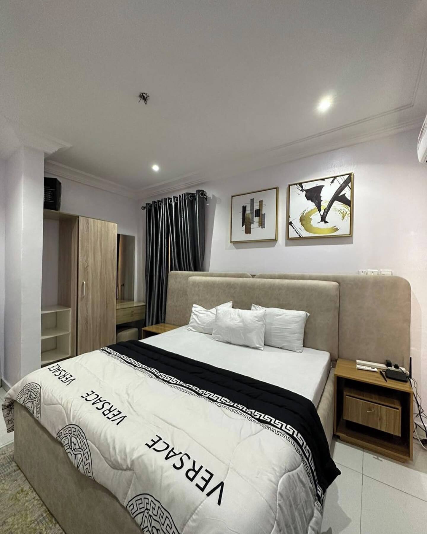 A modern hotel room with a large bed, a wardrobe, a nightstand, and two abstract paintings on the wall.
