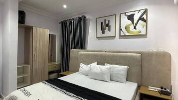 A modern hotel room with a large bed, a wardrobe, a nightstand, and two abstract paintings on the wall.