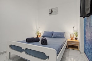 A modern bedroom with a bed, pillows, a bedside table with a lamp, a wall-mounted artwork, and a blue accent wall.