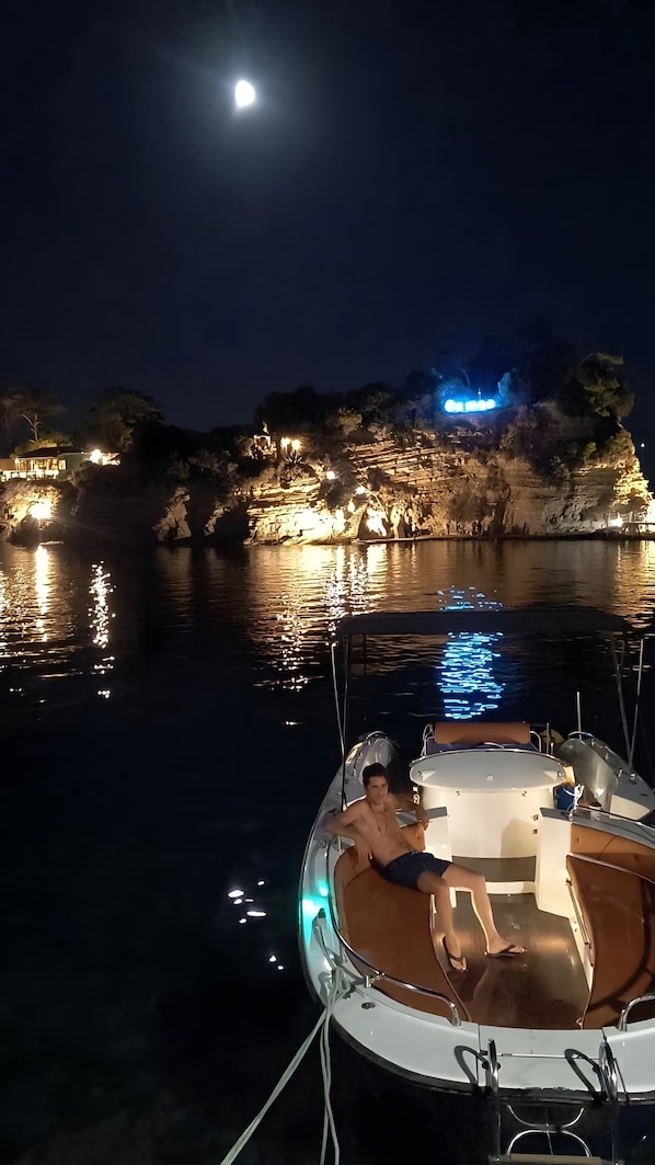 A boat docked at night with a moon in the sky and lights reflecting on the water.