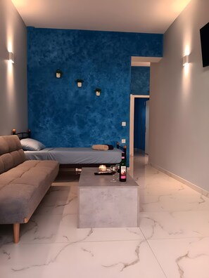 Una camera moderna con una parete blu e strutturata, un letto, un divano, un tavolino da caffè con una bottiglia e un bicchiere, e una piccola pianta.