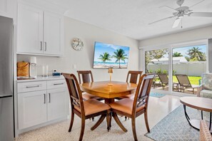 A dining area with a wooden table and chairs, a clock on the wall, and a view of the outdoors through large sliding doors. - Jamaica Royale 106 Beautiful Condo! (Siesta Key)