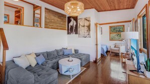 Ein modernes Wohnzimmer mit Holzboden, einem großen grauen Ecksofa, einem runden Couchtisch und Kunstwerken an den Wänden.
