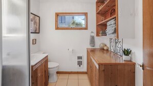 Ein kleines Badezimmer mit Toilette, Waschbecken, Fenster und Holzregalen mit Handtüchern.