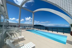 A pool area with lounge chairs and a clear view of the sea. - SA Clube XV  Apto CXV1601 (Santos)