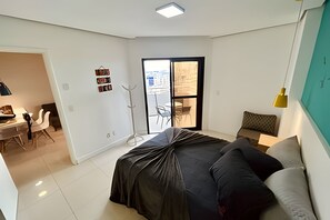 Ein modernes Schlafzimmer mit Bett, Schreibtisch und Stuhl. Ein Balkon bietet Blick auf die Stadt.