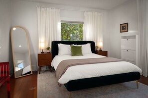 Ein Schlafzimmer mit einem Bett, einem Spiegel, einer Kommode und einem Fenster mit Vorhängen.