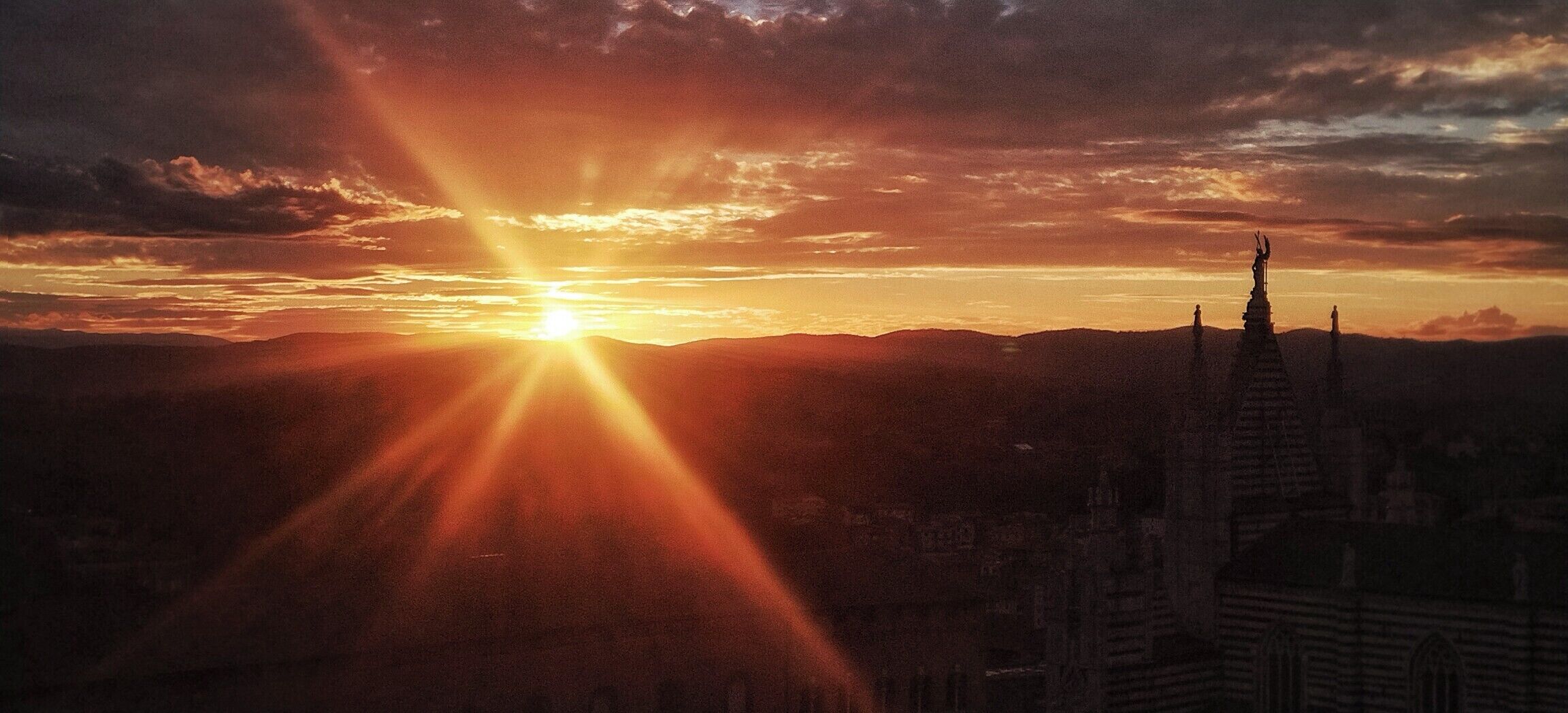 Kaupunkikuva, jossa näkyy selkeästi korkea torni ja auringonlasku.