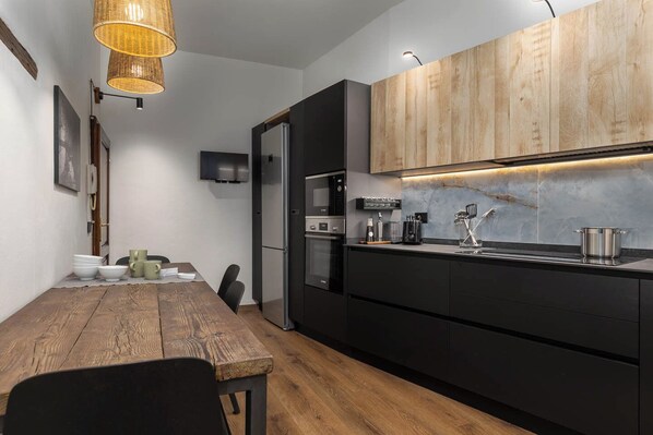 A modern kitchen with black cabinetry, a wooden dining table, and a hanging light fixture.