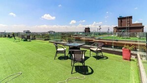 Terraza en la azotea con césped artificial, mobiliario exterior y vistas a la ciudad.