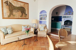 A living room with a sofa, coffee table, and armchairs, a bookshelf, and a kitchen visible through an archway. - Villa Angie by My Villa Collection (Positano)