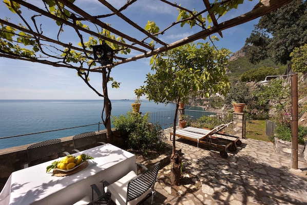 Eine Terrasse mit Esstisch, einer Liege und Blick auf das Meer.