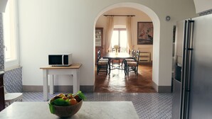 Una cucina con zona pranzo, un forno a microonde su un ripiano, un frigorifero e un tavolo con sedie.