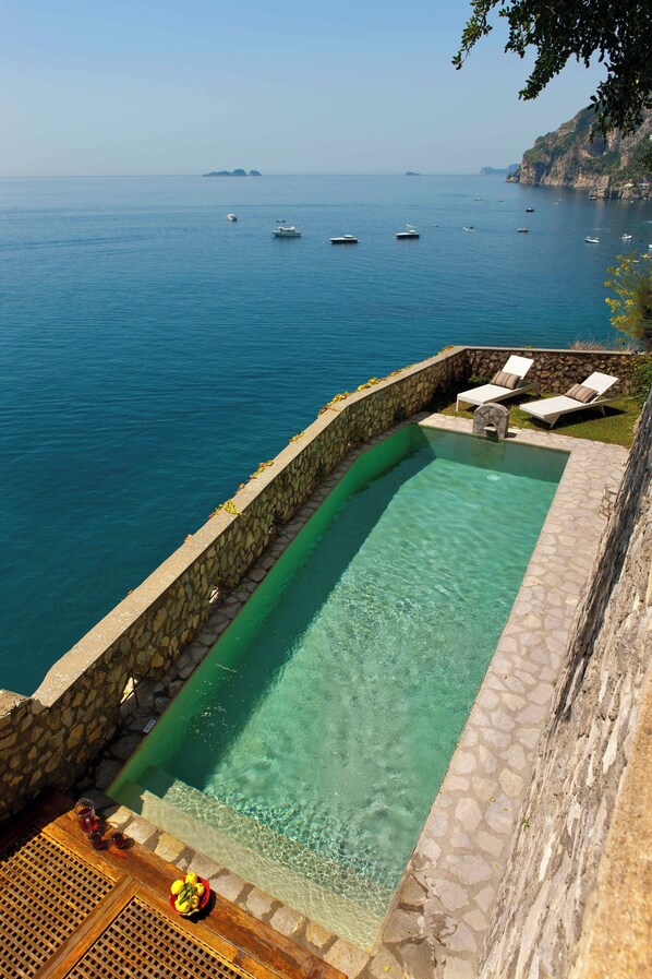 Ein rechteckiger Swimmingpool mit Steinwänden, einer Holzterrasse und Liegestühlen.