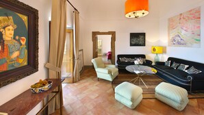 Un soggiorno con divano, poltrone, poggiapiedi, tavolino da caffè, un quadro e una grande lampada a sospensione arancione.