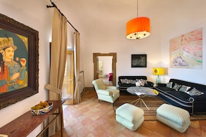 Ein Wohnzimmer mit einer Couch, Sesseln, Hocker, einem Couchtisch, einem Gemälde und einer großen orangefarbenen Pendelleuchte.