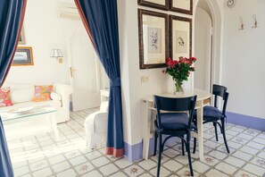 Ein Zimmer mit einem weißen Sofa, einem Glastisch, einem Esstisch mit Stühlen und einer Vase mit Blumen.