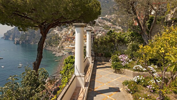 Eine Küstenstadt mit einer Steintreppe, Bäumen und Blick auf das Meer und die Bebauung.