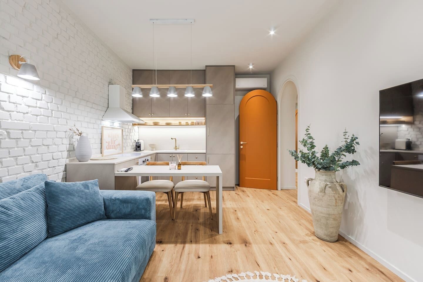A modern kitchen with a dining area, a blue sofa, and a large vase with plants.