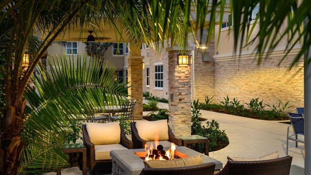 An outdoor patio area with wicker furniture, a fire pit, and palm trees.