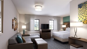 A hotel room with a sofa, a bed, a TV, and a desk with a lamp.