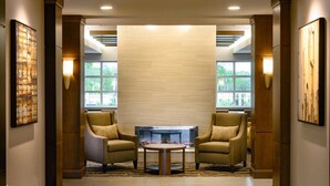 A lobby with two armchairs, a coffee table, a fireplace, and large windows.