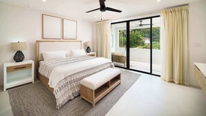 A bedroom with a bed, bedside tables, a bench, a ceiling fan, and a view of greenery through a sliding door. - Walk to Beach, New Elegant 2BR Villa with Pool! (Lower Carlton)