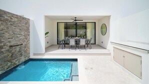A modern outdoor pool area with a dining table and chairs, a ceiling fan, and a brick wall. - Walk to Beach, New Elegant 2BR Villa with Pool! (Lower Carlton)