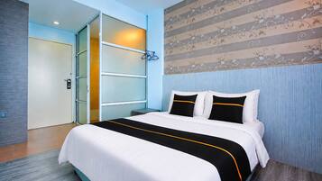 A hotel room with a bed, a door, and a wall with a floral pattern.