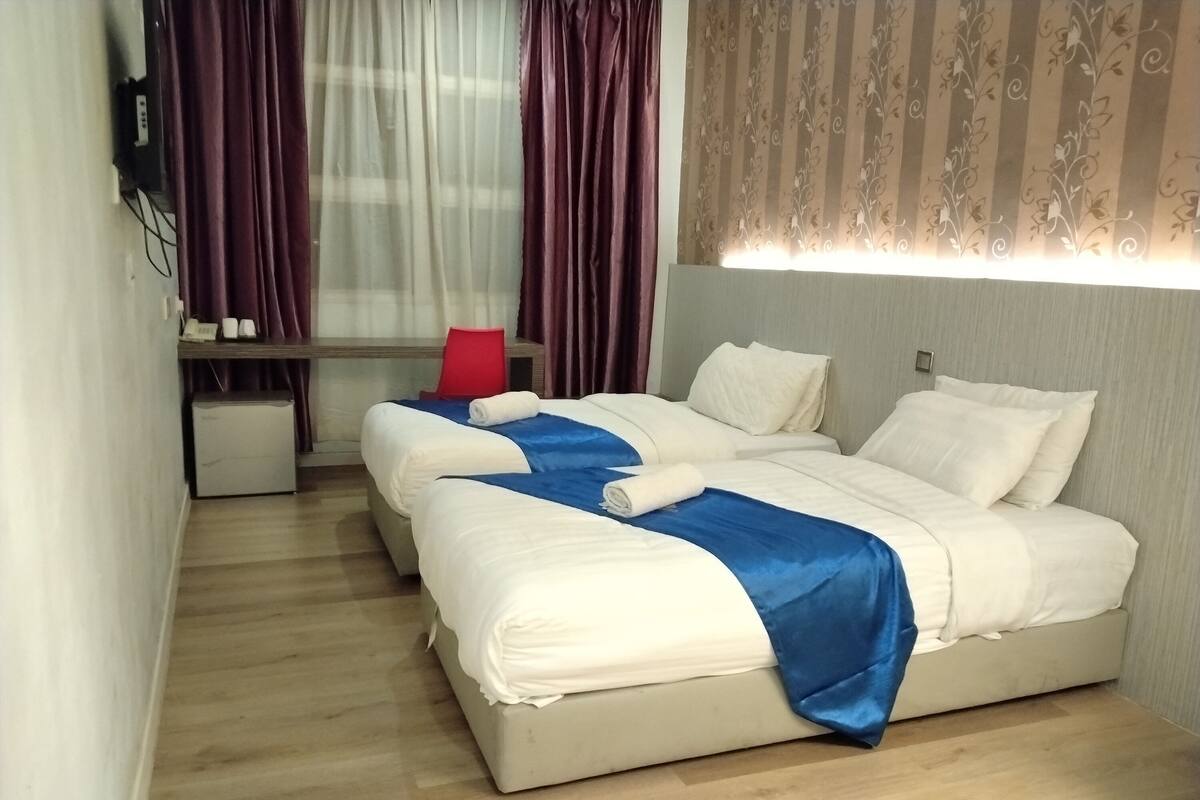 A hotel room with two beds, a desk, a red chair, and a small refrigerator.