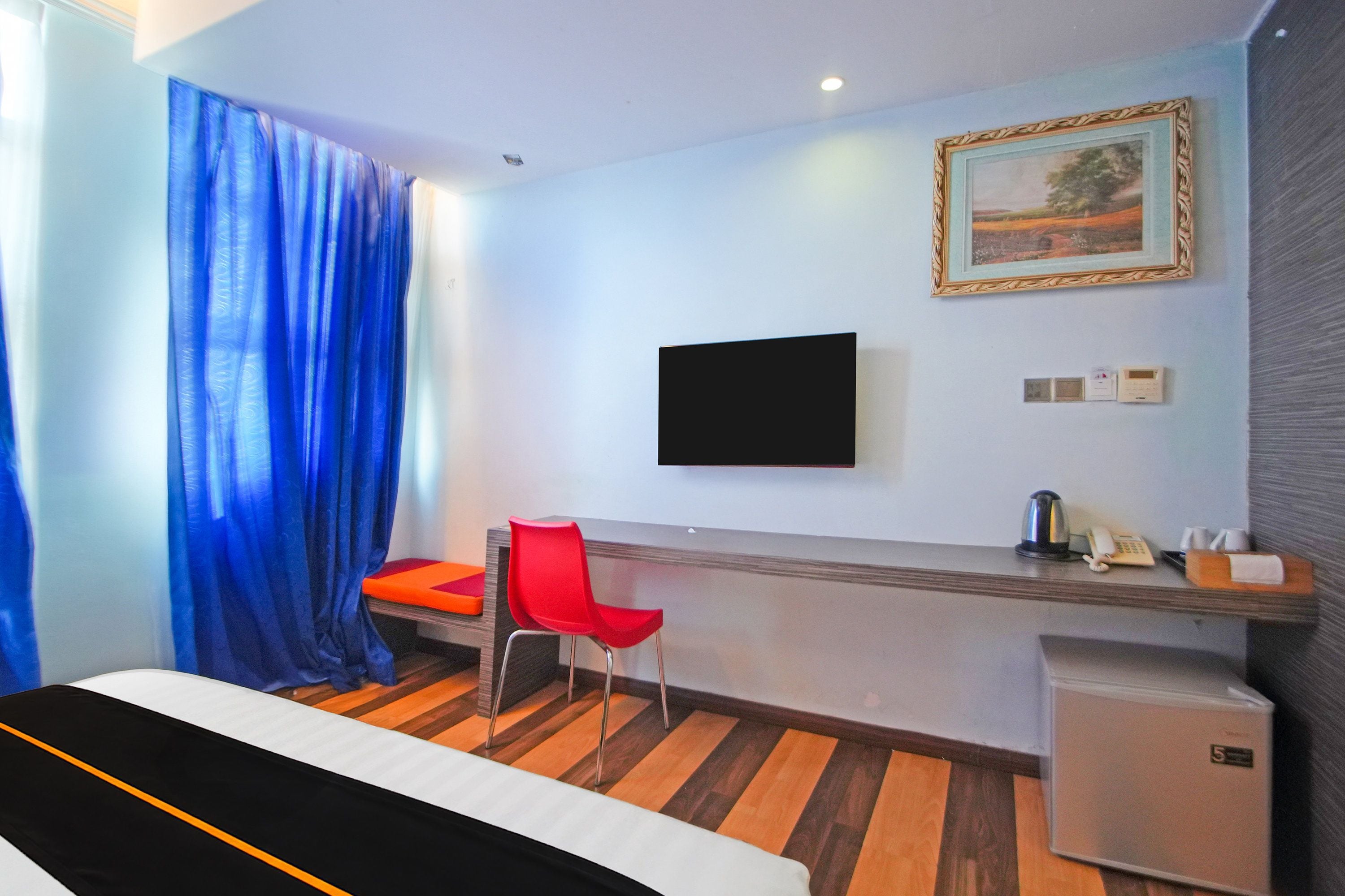 Ein Hotelzimmer mit einem Bett, einem Schreibtisch mit Stuhl, einem an der Wand befestigten Fernseher und einem kleinen Kühlschrank.