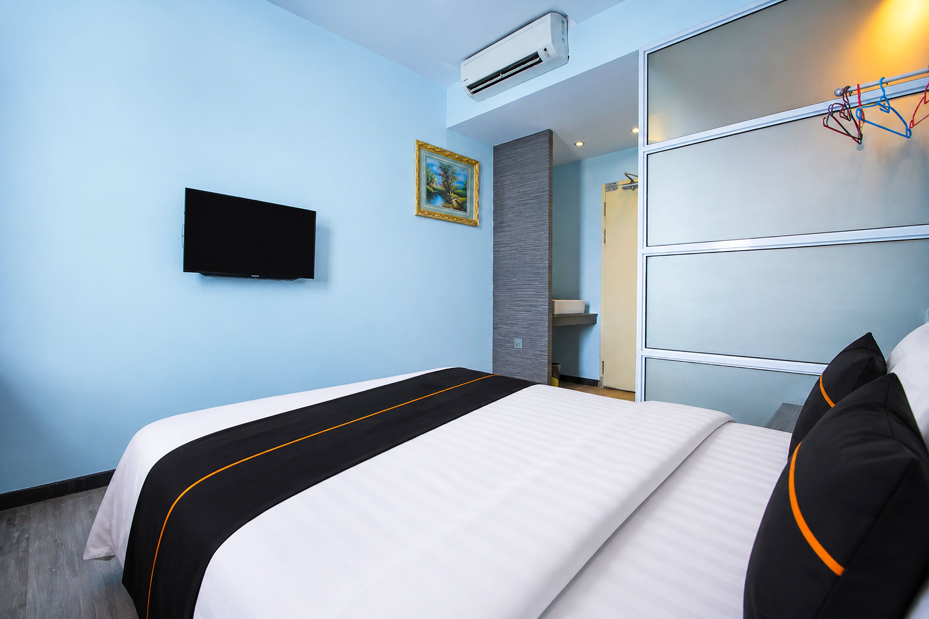 A hotel room with a bed, a television, a wardrobe, and an air conditioning unit.