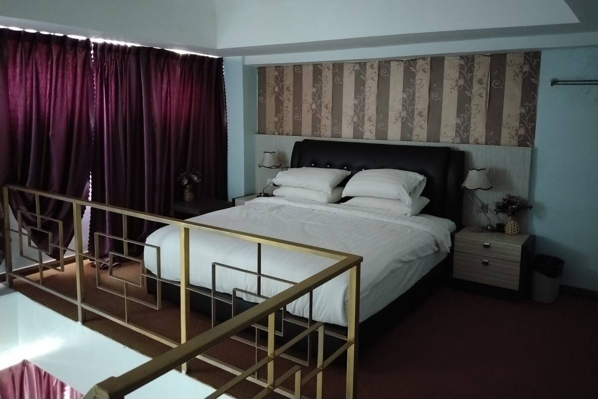A bedroom with a bed, a nightstand, a lamp, and a window with curtains.