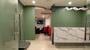 Zona de recepción de hotel con mostrador de mármol, paredes verdes y suelo de baldosas.