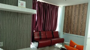 Una habitación con un sofá rojo, una mesa de vidrio, una pared blanca con un cartel de 'No Fumar' y una cortina estampada.