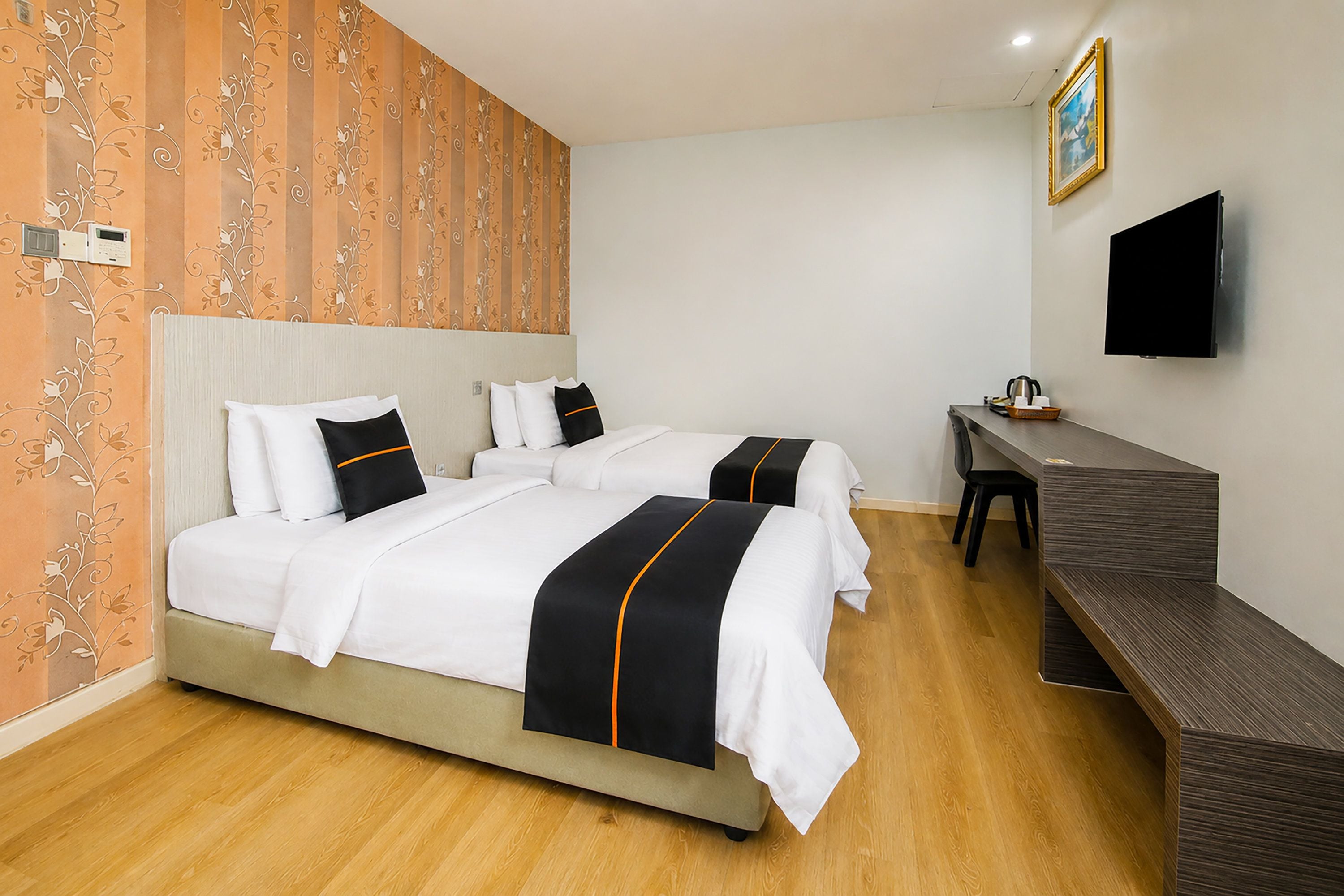 A hotel room with two beds, a desk, a chair, a flat-screen TV, and a wooden floor.