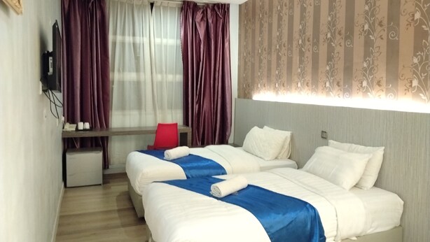 Habitación de hotel con dos camas, un escritorio, una silla y un ventanal con cortinas.