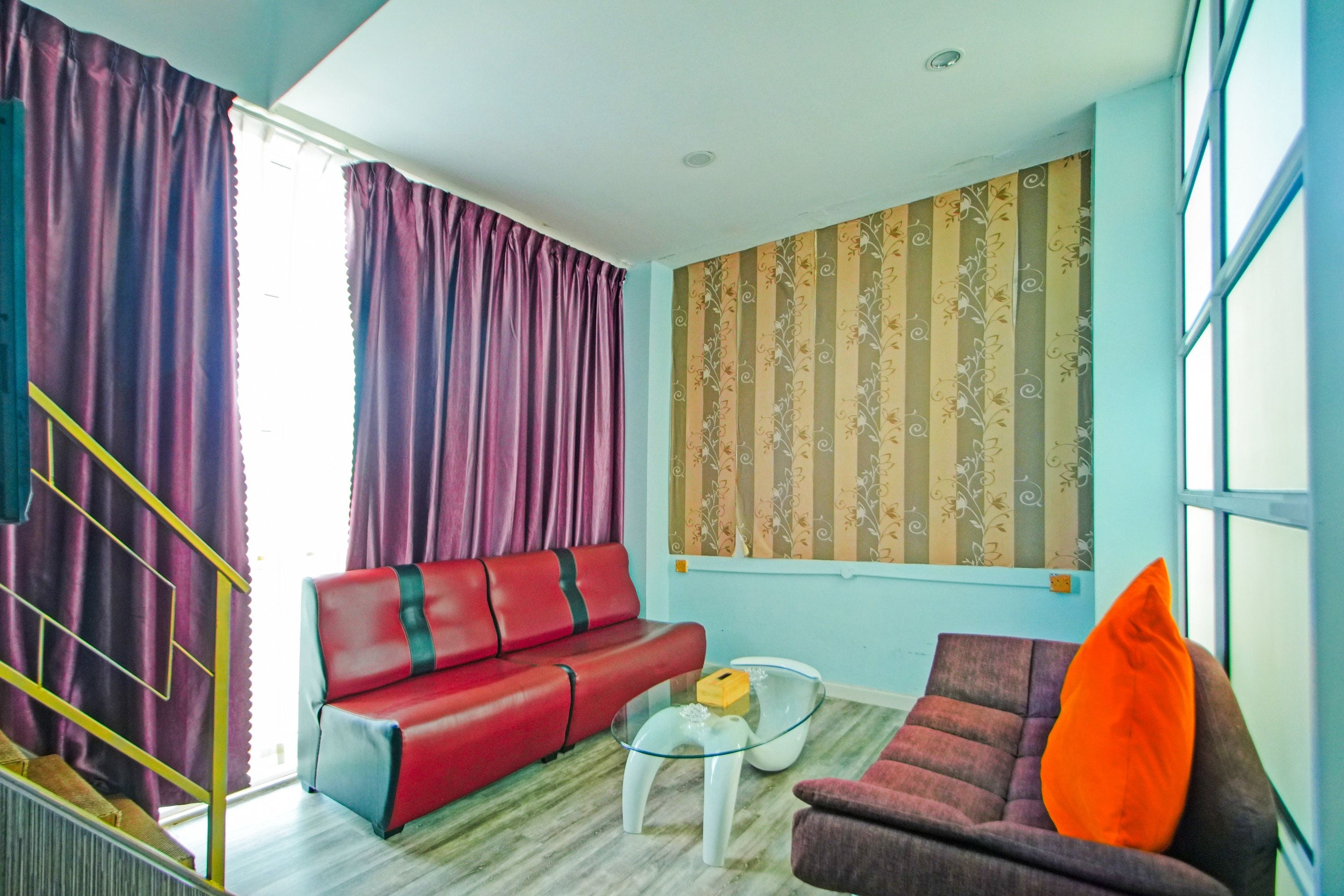 A living room with a red sofa, a smaller armchair, a glass coffee table, and a window with striped curtains.