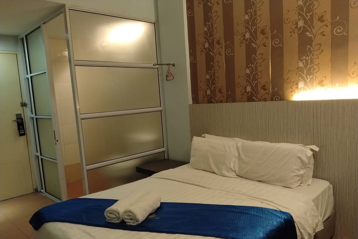 A hotel room with a bed, a wardrobe, and a wall with a floral pattern.