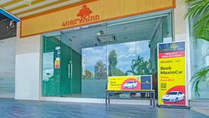 Un hostal del 4 de julio con entrada de vidrio, un anuncio del servicio de transporte MaxximCar y un cartel que indica un punto de recogida y devolución.