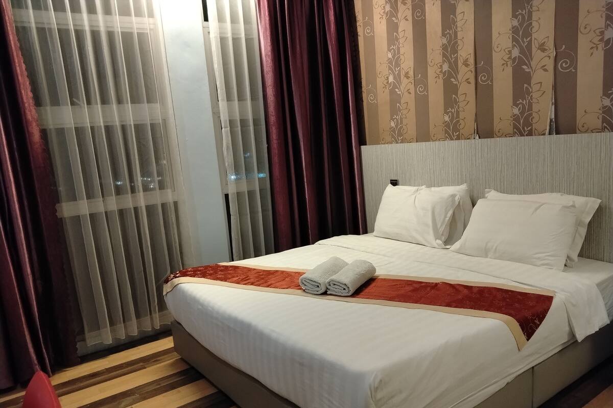 A hotel room with a bed, curtains, and a striped wallpaper pattern.