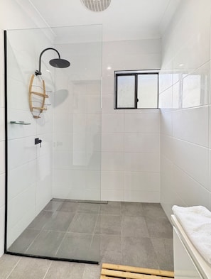 Ein modernes Badezimmer mit Duschkabine aus Glas, einem Holzregal und einem Fenster.