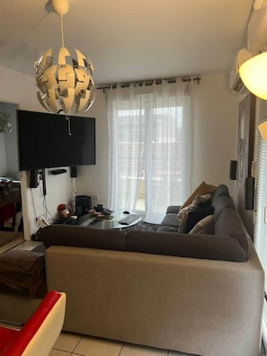 A living room with a sofa, a coffee table, a flat-screen TV, and a unique spherical chandelier. - Marne and Magic (Noisy-le-Grand)