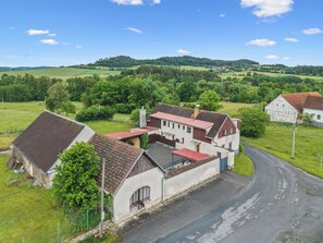 Un bâtiment rural avec un toit rouge, entouré de champs verdoyants et de collines.