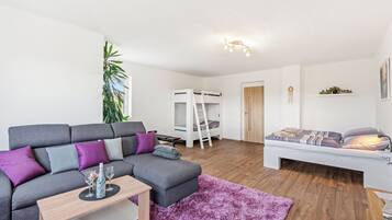 Un salon moderne avec un canapé gris, une petite table, un tapis violet, un lit superposé et une échelle blanche.