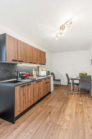 A modern kitchen with wooden cabinets, a black countertop, and a dining area with a table and chairs.
