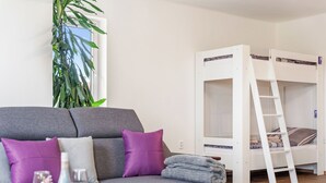 A room with a grey sofa, a white bunk bed, a wooden table with a vase and glasses, and a large plant. - Happy Home by Interhome (Hradesice)