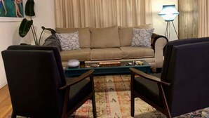 A living room with a sofa, two armchairs, a coffee table, a ceiling fan, a lamp, and a patterned rug.