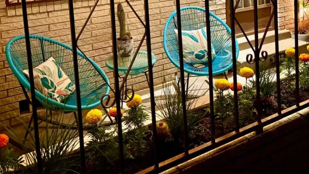 A gated patio with two wicker chairs, a cactus, and a variety of flowers.