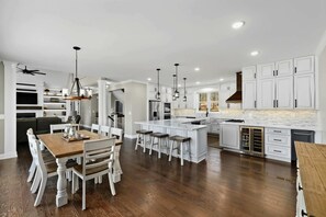 A modern kitchen with white cabinetry, a wooden dining table, and bar stools. - Waterfront Retreat Lakefront Game Room Dock (Bumpass)